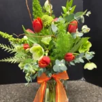 red and white flowers with greenery and an orange ribbon in a glass vase