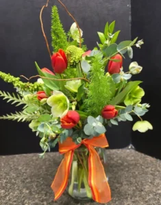 red and white flowers with greenery and an orange ribbon in a glass vase