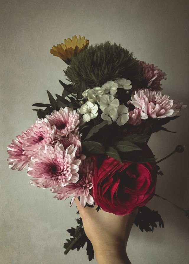 A vase filled with a colorful mix of red, pink, and yellow flowers with an assortment of greens.