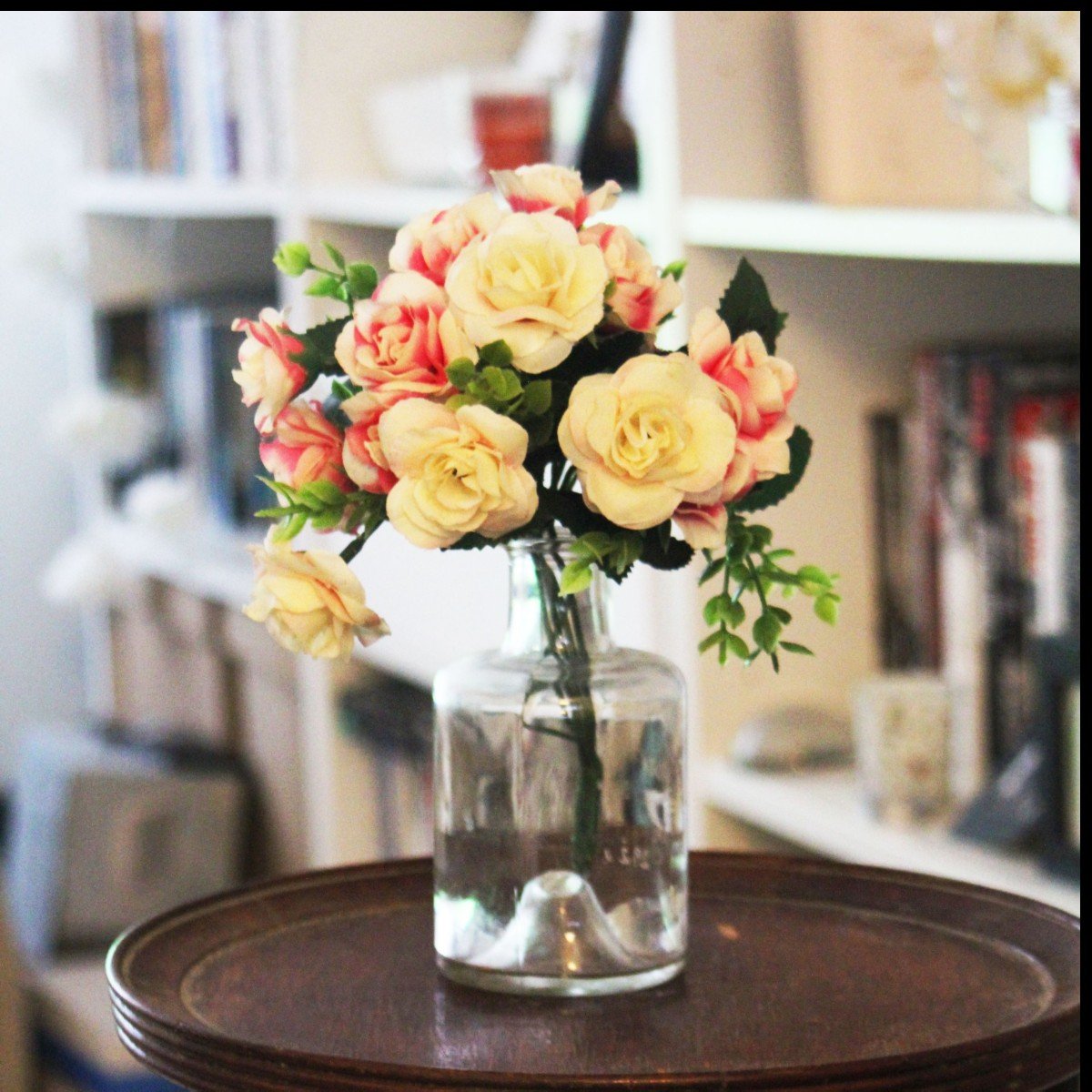 Cream and yellow flowers arranged in a clear glass vase on a wooden table.