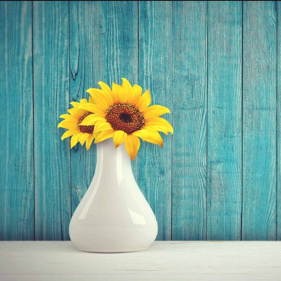 sunflowers in a vase sitting in front of a blue wooden fence